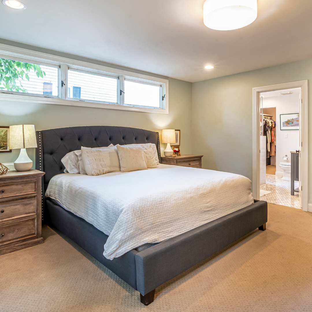 Modern kitchen with wood cabinets, black granite countertops, stainless steel appliances, pendant lighting, and a curved island with two barstools. Large windows provide natural light and a view of trees outside.
